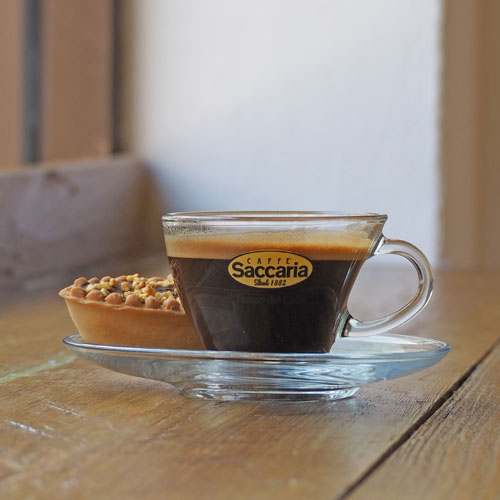 A glass cup of freshly made espresso topped with a good crema and with an Italian pastry on the side.