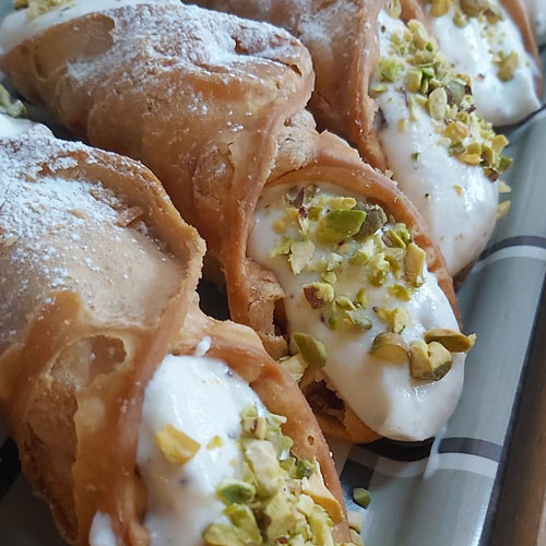 A close up of Sicilian cannoli with a creamy ricotta filling & topped with crushed pistachios.